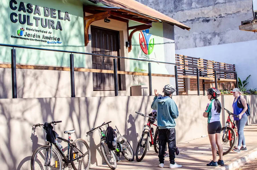 Fachada de la Casa de la Cultura de Jardín América con ciclistas en la vereda