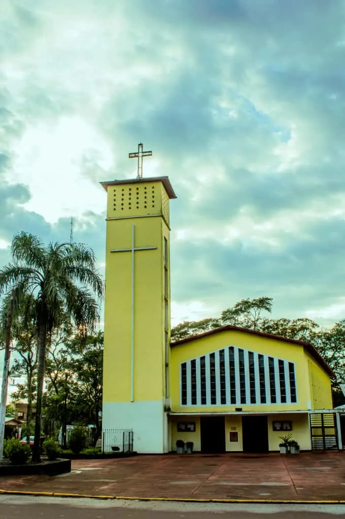 Fachada exterior de la Parroquia Cristo Redentor de Jardín América con su torre y cielo nublado