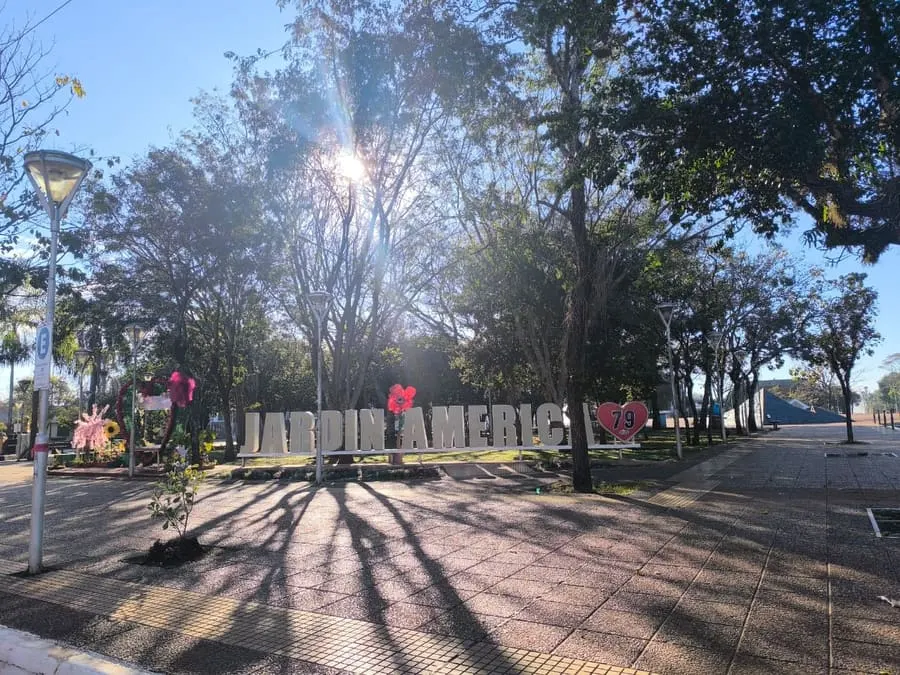 Plaza Colón de Jardín América con el cartel de la ciudad y arboledas bajo la luz del sol
