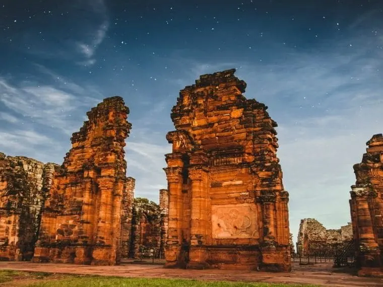 Reducciones Jesuíticas de San Ignacio Mini iluminadas bajo un cielo estrellado, con las torres de piedra roja al fondo