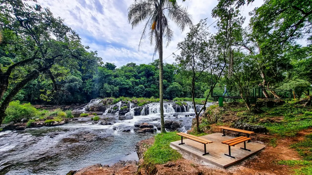 Vista panorámica de las cascadas con banco de madera y palmera al frente