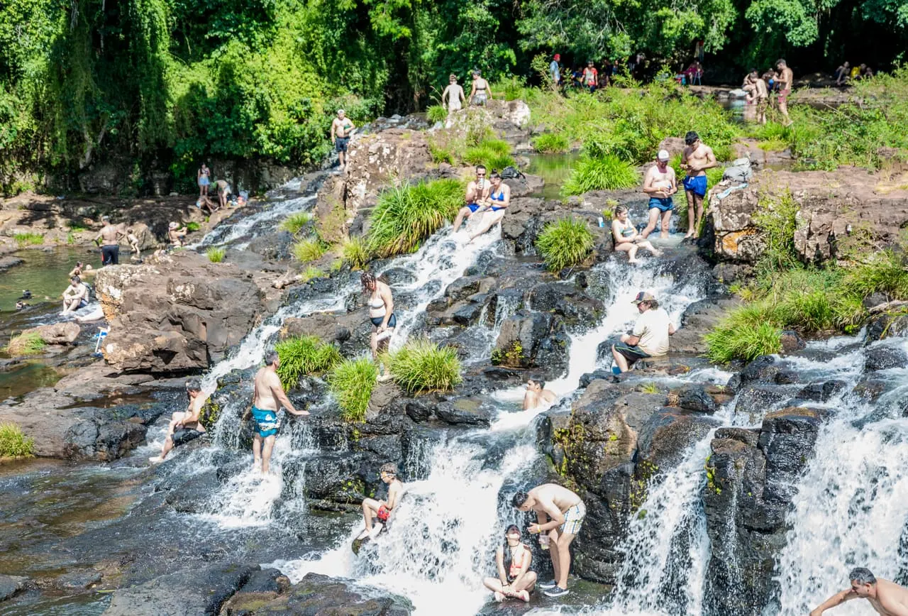 Visitantes sentados sobre las rocas entre las cascadas en un día soleado